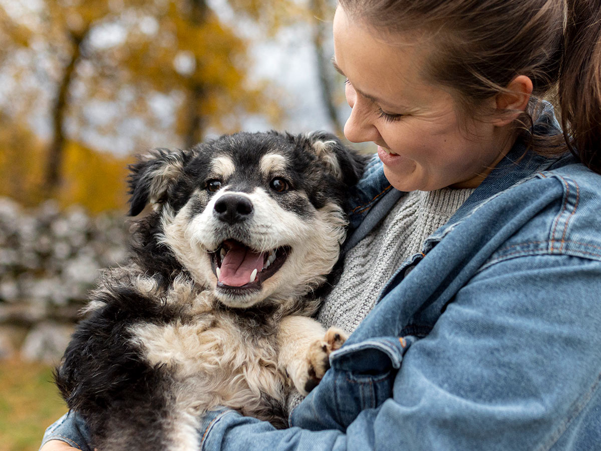 cheerful woman holding an excited black and white puppy at the park